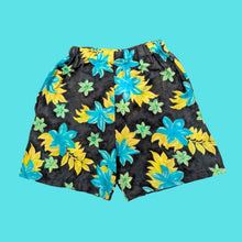 Load image into Gallery viewer, A pair of navy sustainable shorts with a vibrant tropical floral print featuring large teal and yellow flowers, small green flowers, and green leaves
